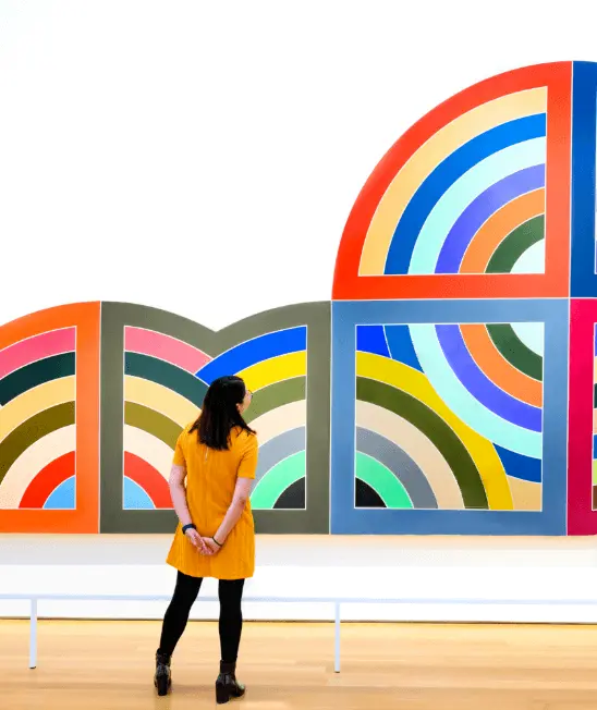 A woman observing artwork from Frank Stella on display at the North Carolina Museum of Art