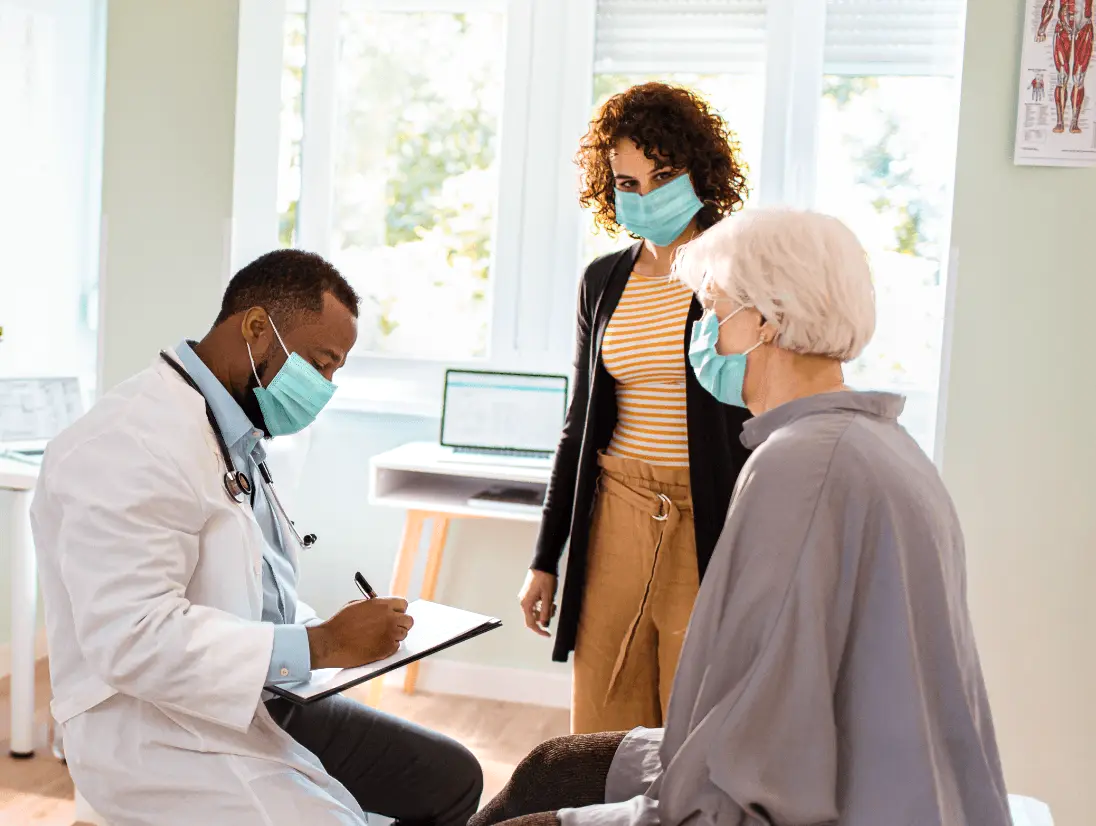 A woman with a family member consults with her doctor in a medical office setting